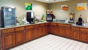 A hotel kitchen with wooden cabinets, a refrigerator, a coffee machine, and a waffle maker.