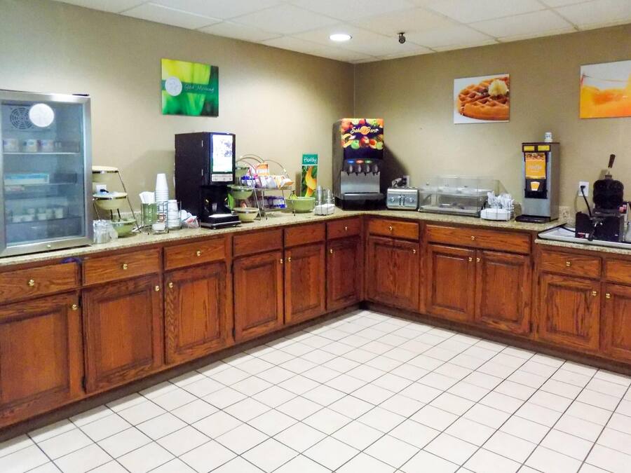 A hotel kitchen with wooden cabinets, a refrigerator, a coffee machine, and a waffle maker.