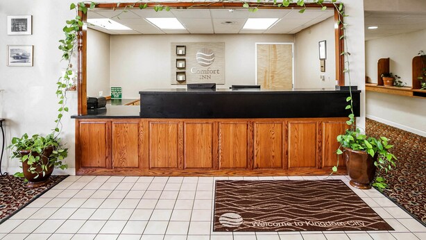 A reception desk with a wooden panel design, a framed artwork above it, and a sign reading "Comfort Inn". - Quality Inn Kingdom City I-70 (Kingdom City)