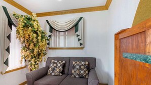 A room with a grey sofa, patterned cushions, a hanging floral arrangement, and a window with curtains. - Econo Lodge Inn & Suites Near Lackland AFB (San Antonio)