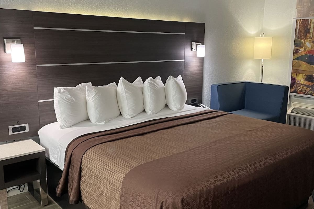 A hotel room with a large bed, a bedside table, a chair, a lamp, and a wall-mounted light fixture.