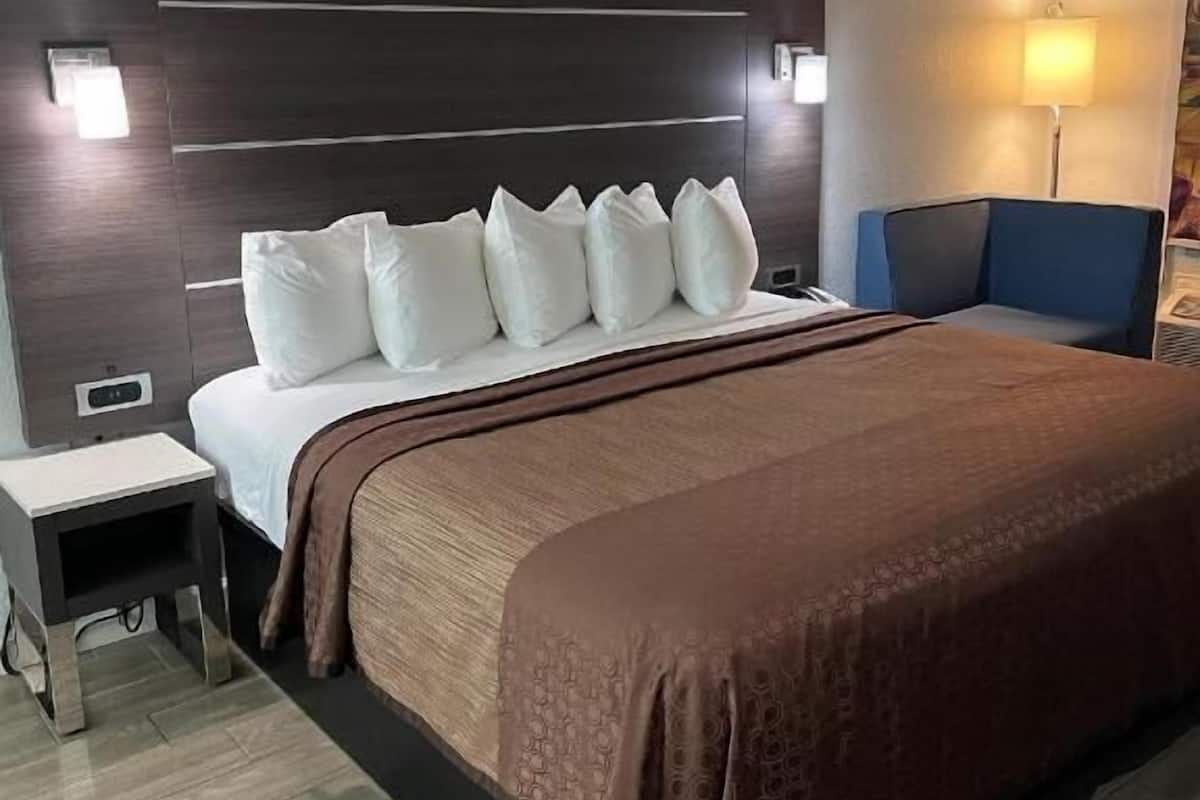 A hotel room with a large bed, a bedside table, a lamp, and a chair.