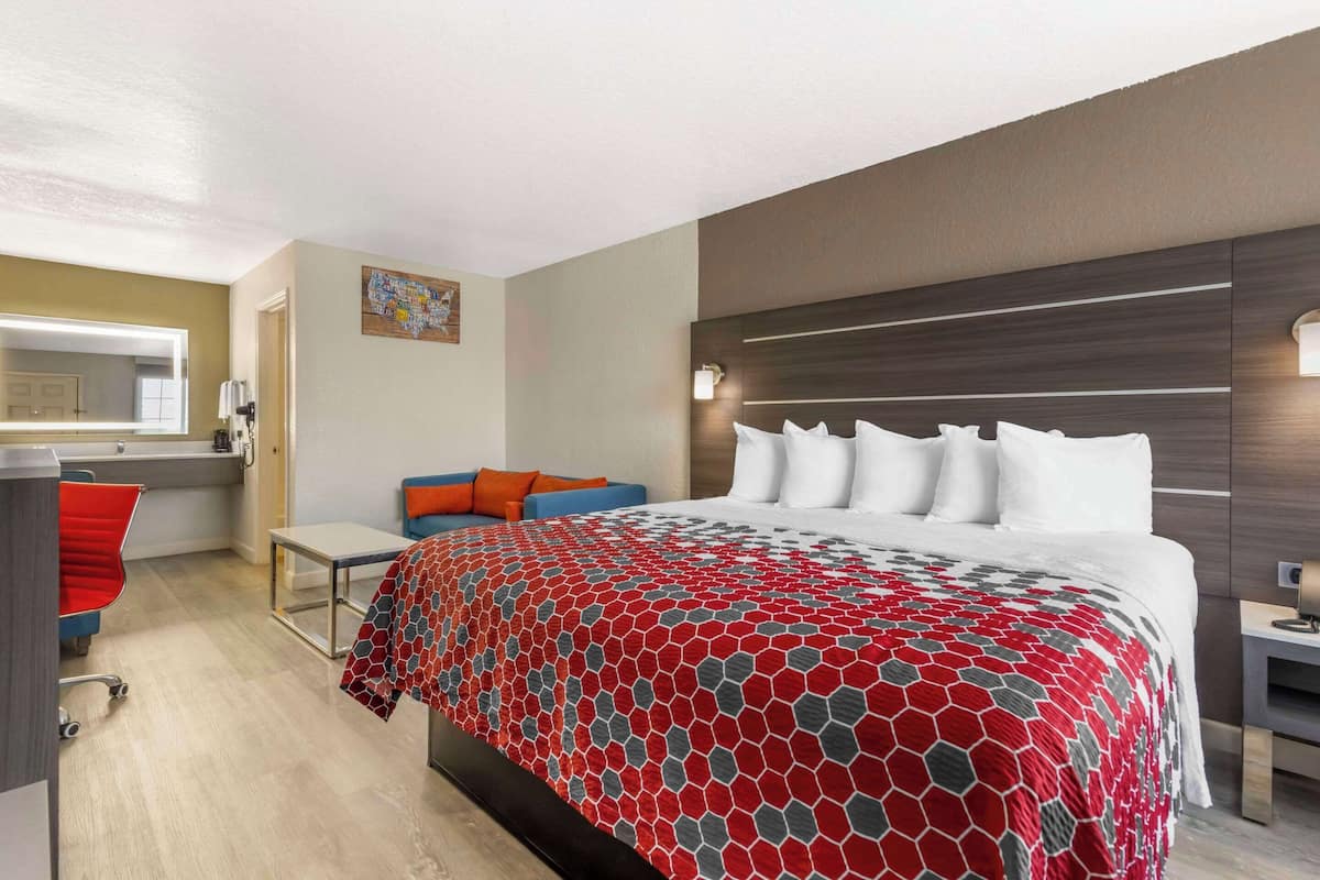 A hotel room with a large bed, a desk, a chair, and a small table.