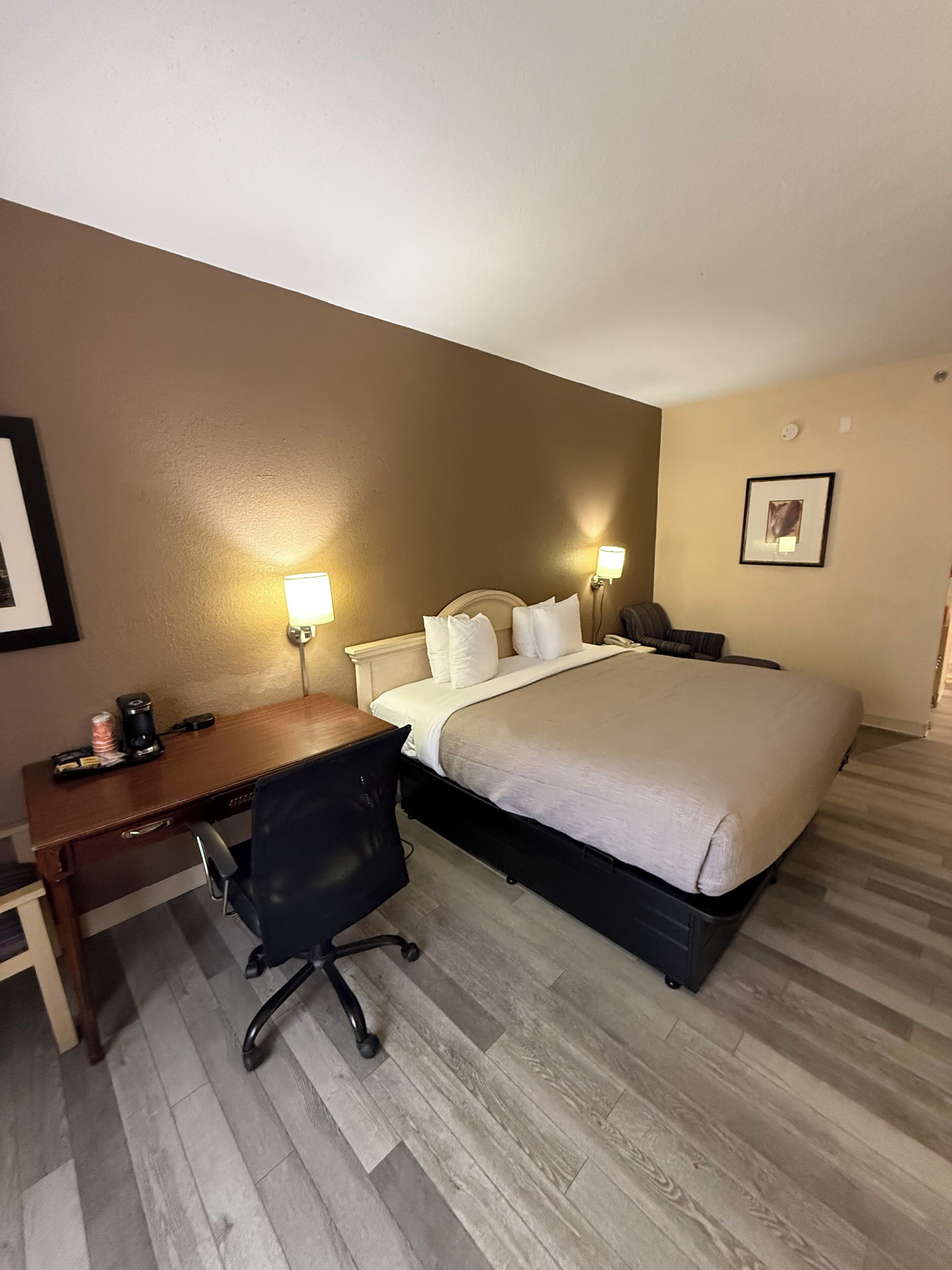 A hotel room with a bed, desk, chair, and two wall-mounted lamps.