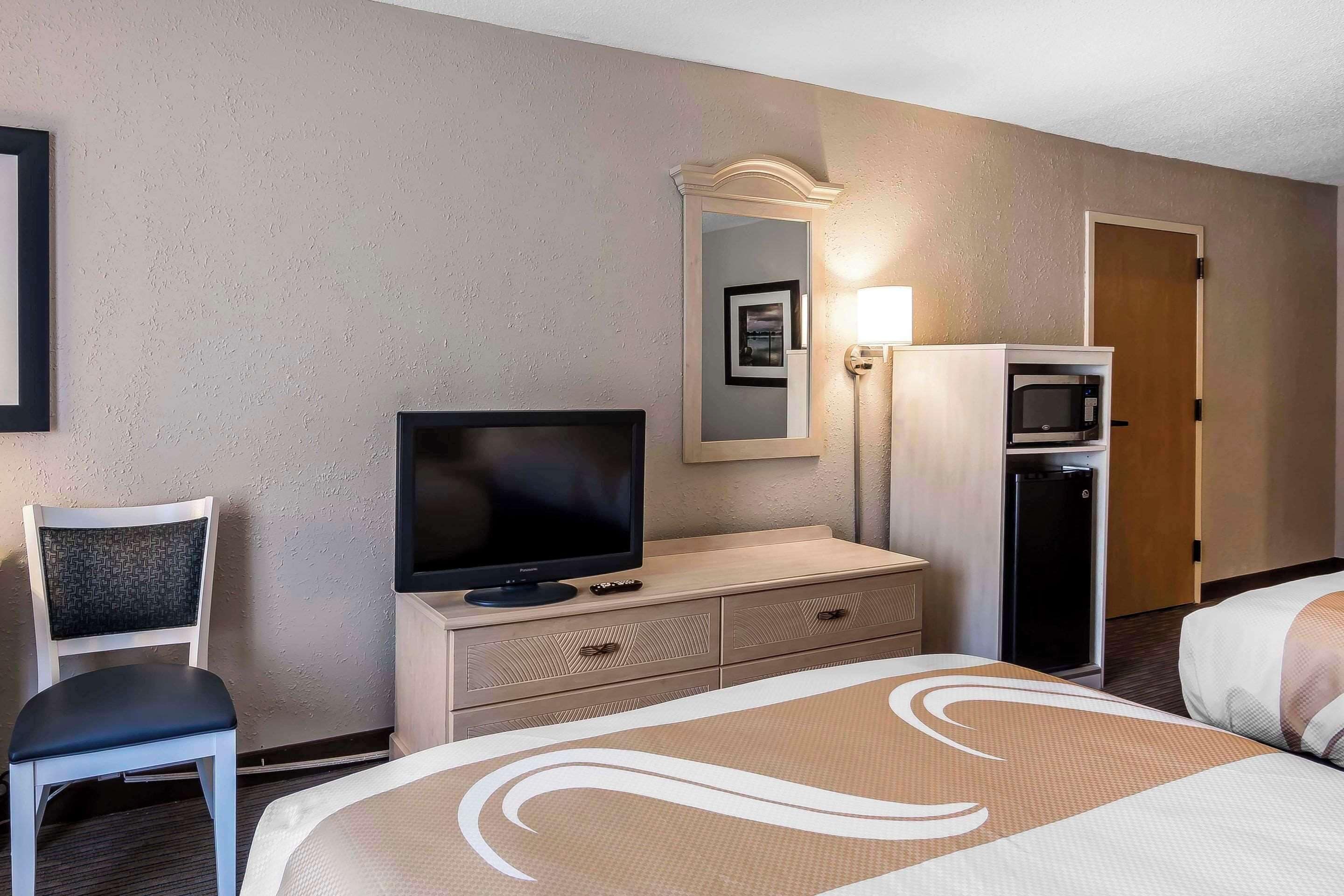 A hotel room with a bed, a television on a dresser, a microwave, a refrigerator, a chair, and a mirror.