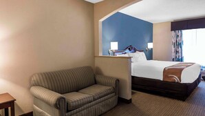 Ein Hotelzimmer mit einem gestreiften Sofa, einem Bett mit brauner Kopfteil, einem großen Spiegel und einem Fenster mit Vorhängen.