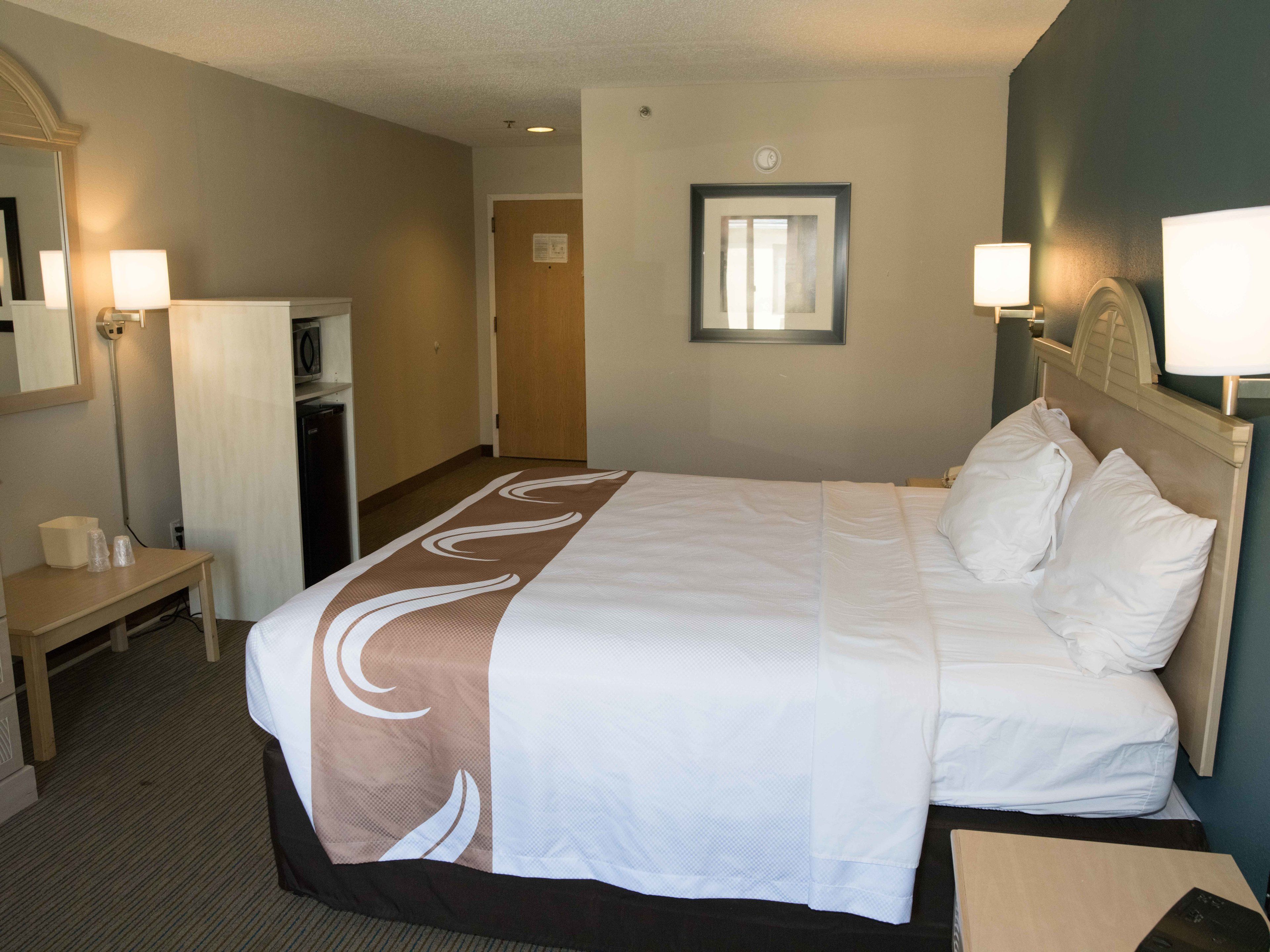 Una habitación de hotel con una cama grande, lámparas de noche, un escritorio y un espejo.