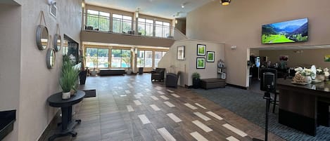A spacious lobby with a high ceiling, a chandelier, a large TV screen, and a staircase leading to an upper level.