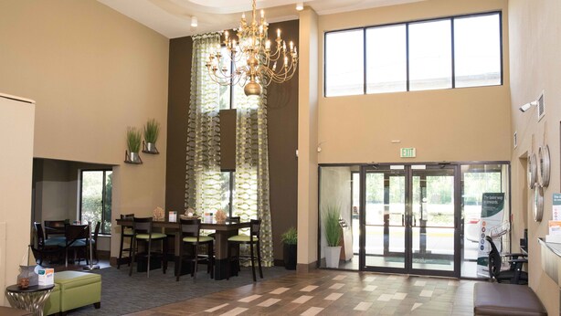 Eine geräumige Lobby mit hoher Decke, einem Chandelier, einem Essbereich mit Tisch und Stühlen und einem großen Fenster, das für natürliches Licht sorgt.