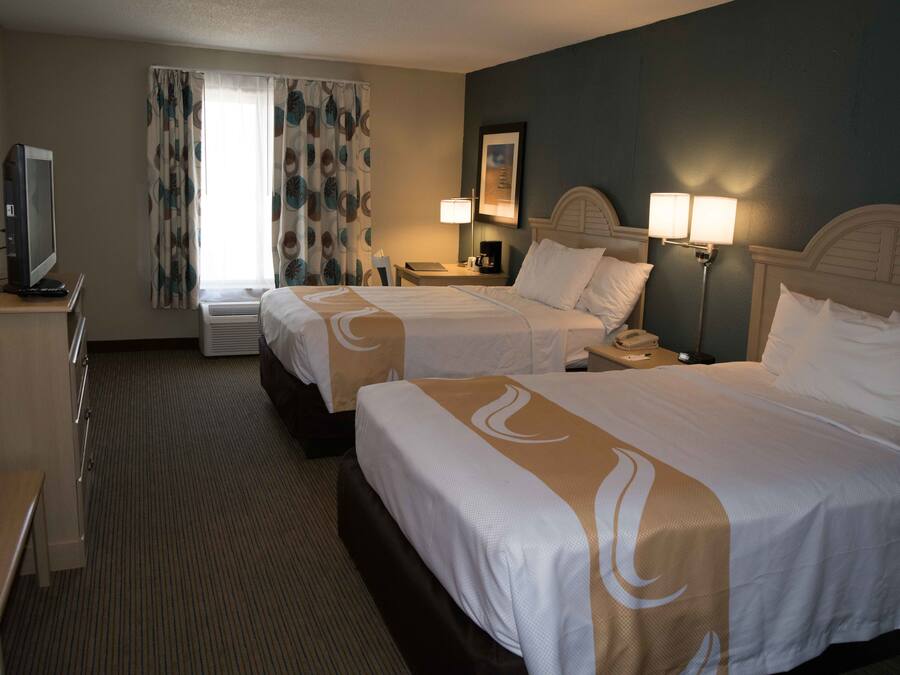 A hotel room with two beds, a desk, a TV, a lamp, and a painting on the wall.