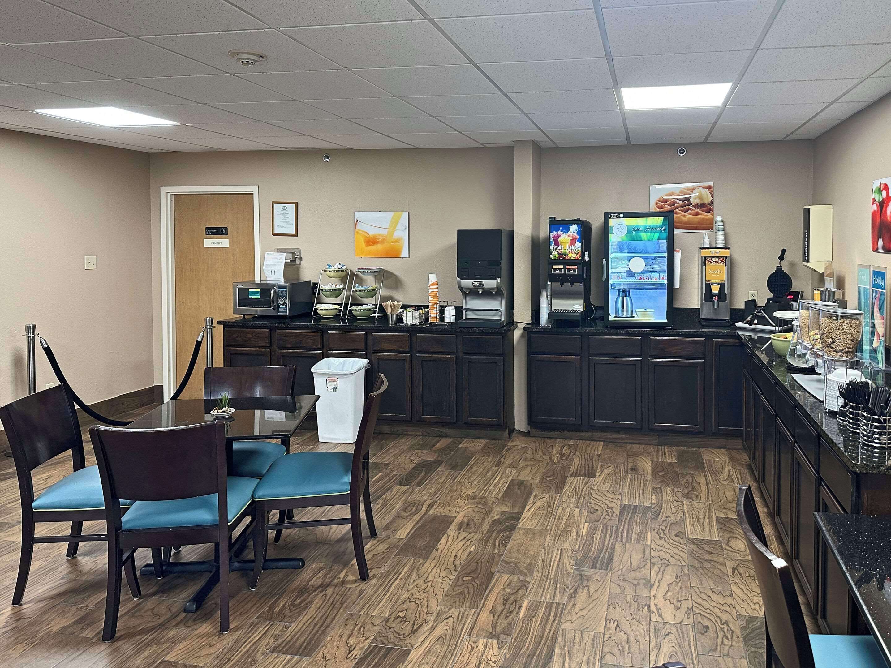 A hotel room with a wooden floor, a dining area with a table and chairs, a kitchenette with a microwave, coffee maker, and a TV.