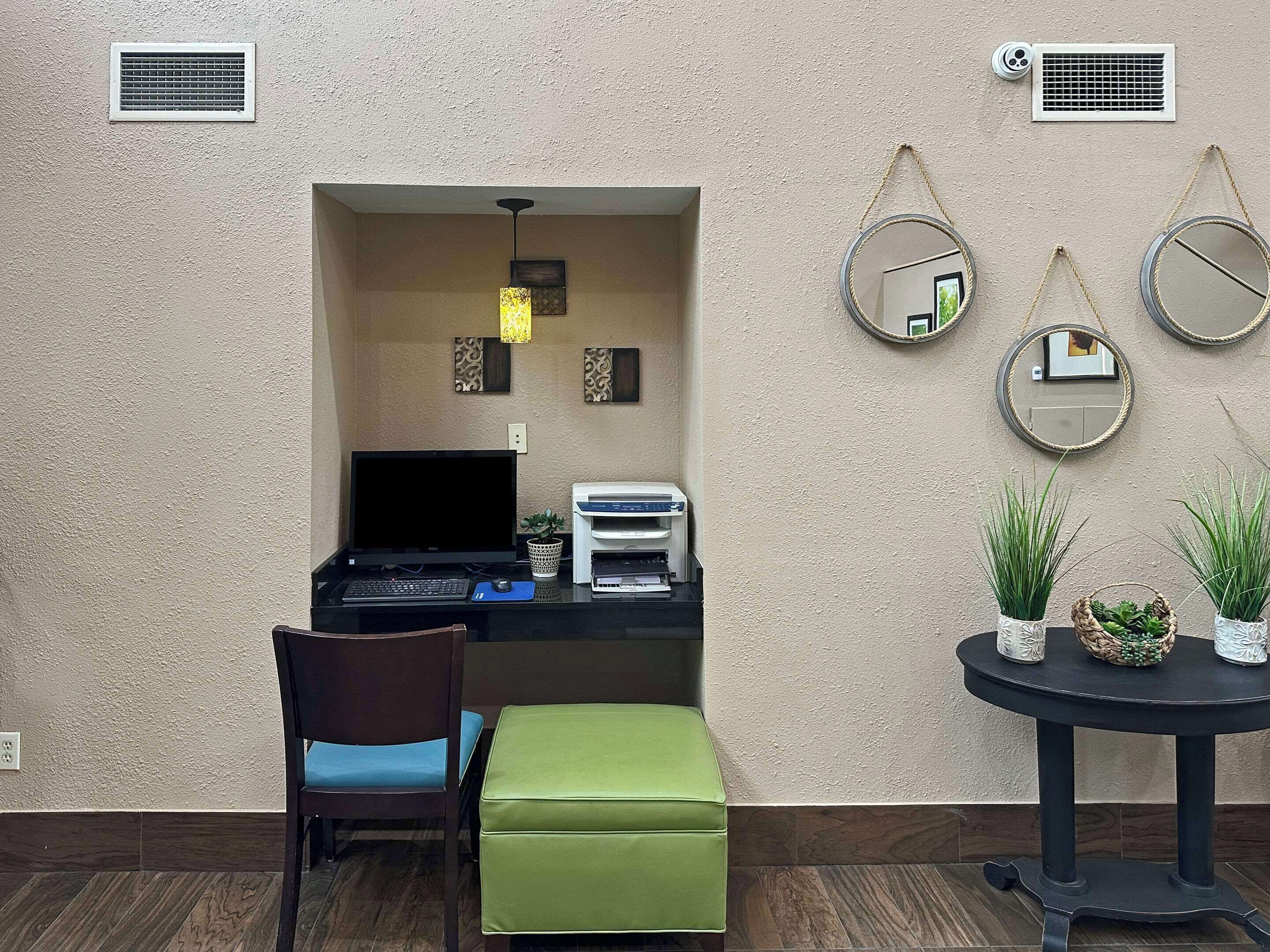 Un espacio de trabajo funcional con escritorio, silla y ordenador, una mesita con plantas y espejos decorativos en la pared.