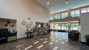 Eine großzügige Lobby mit hoher Decke, einem Empfangsbereich, einer Sitzgelegenheit und großen Fenstern mit Blick ins Freie.
