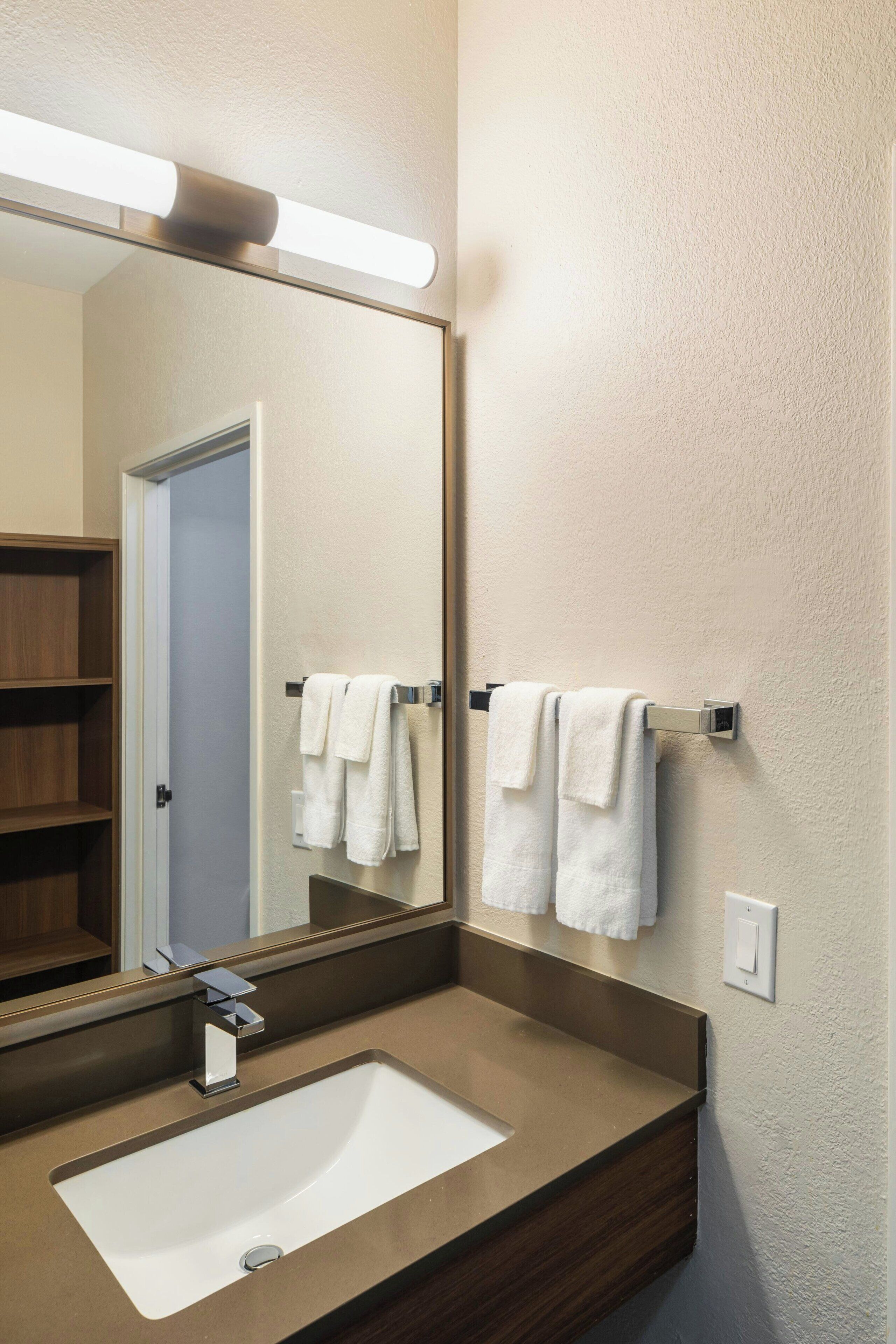 A bathroom with a large mirror, a sink, and two towels hanging on a towel rack.