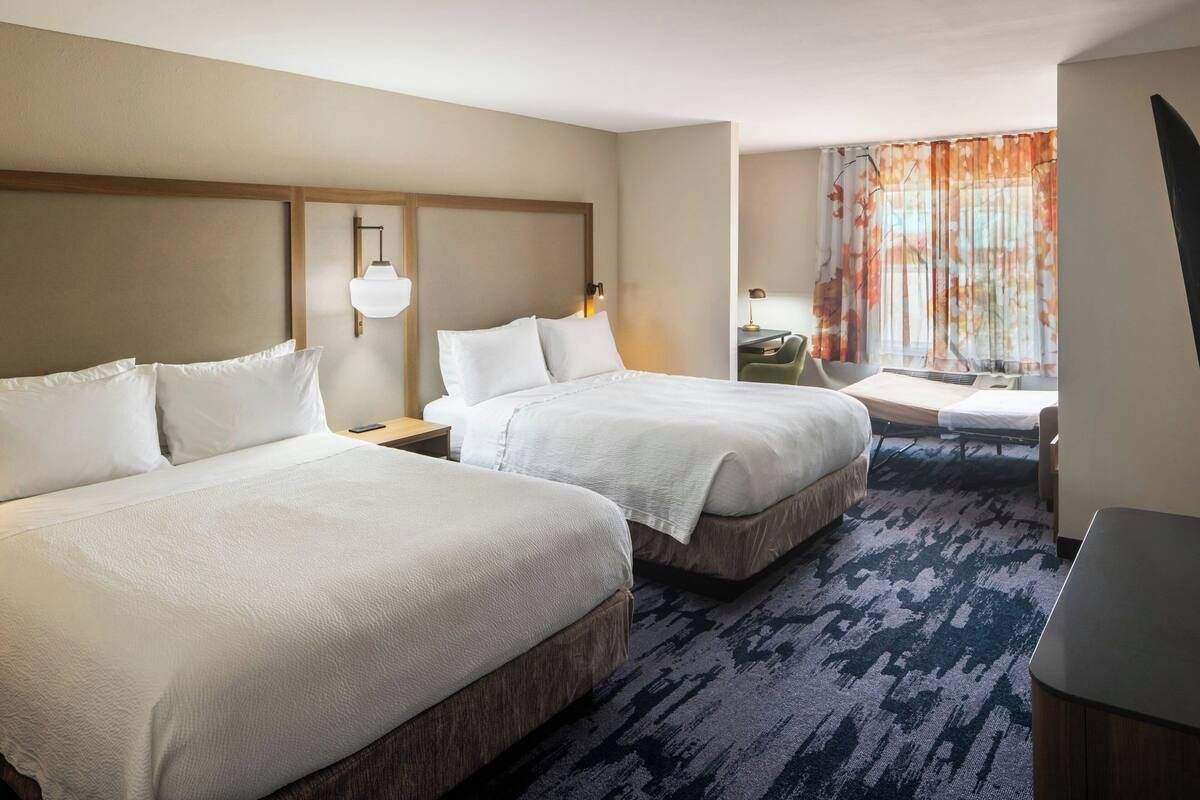 A hotel room with two beds, a desk, a chair, a small table, and a window with curtains.