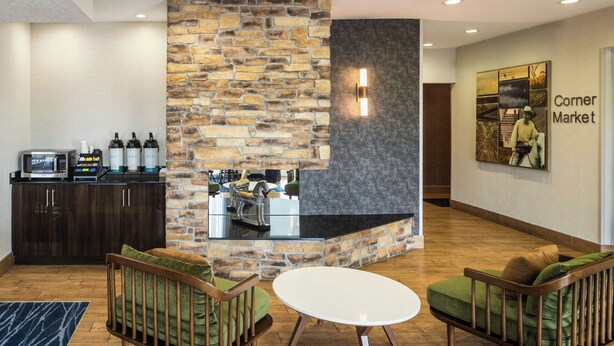 A lobby with a stone wall, a coffee station, two green sofas, and a white table. - Fairfield Inn by Marriott Richmond (New Paris)