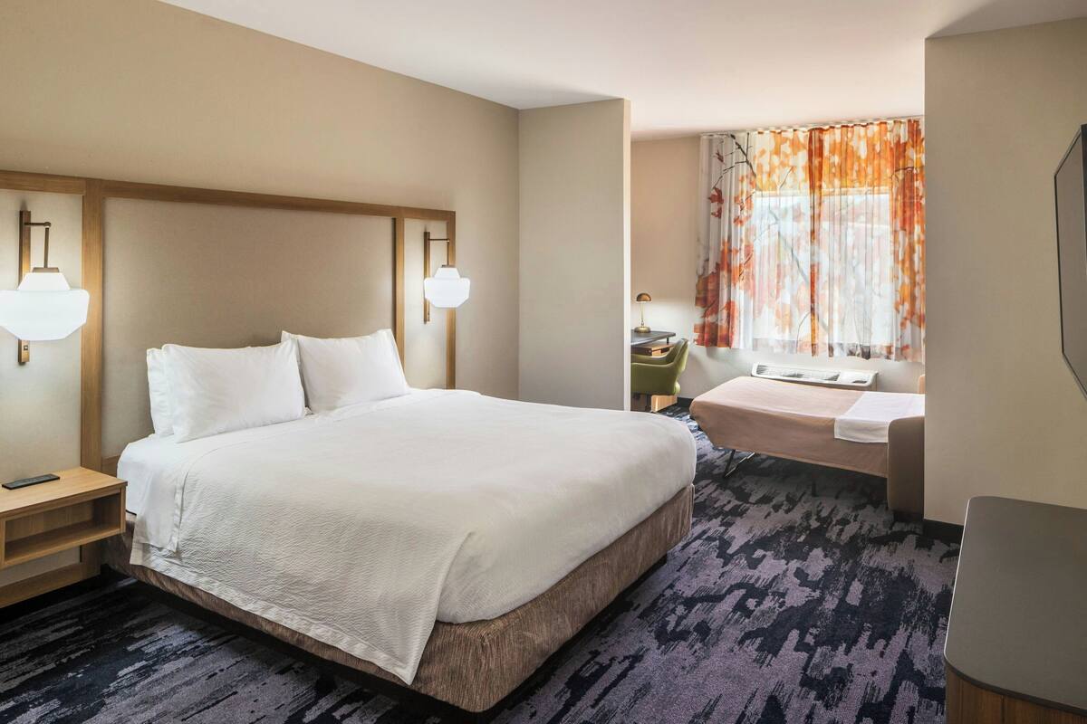 A hotel room with a large bed, bedside tables, a desk, and a window with curtains.