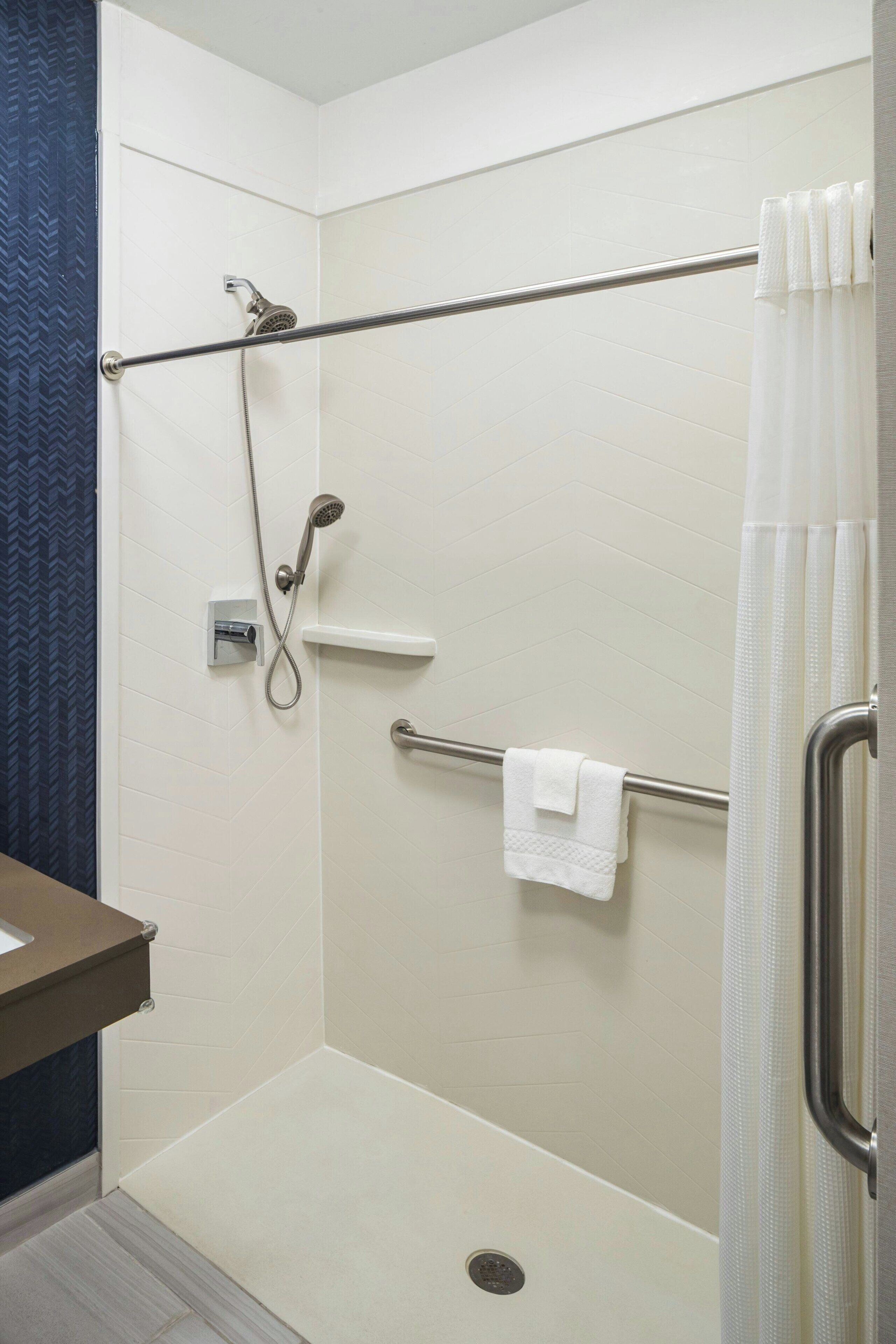 A shower area with a handrail, a towel rack, and a showerhead.