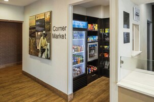 Un mercado de barrio con secciones de alimentos refrigerados y no refrigerados, una máquina expendedora y una pared con carteles informativos.