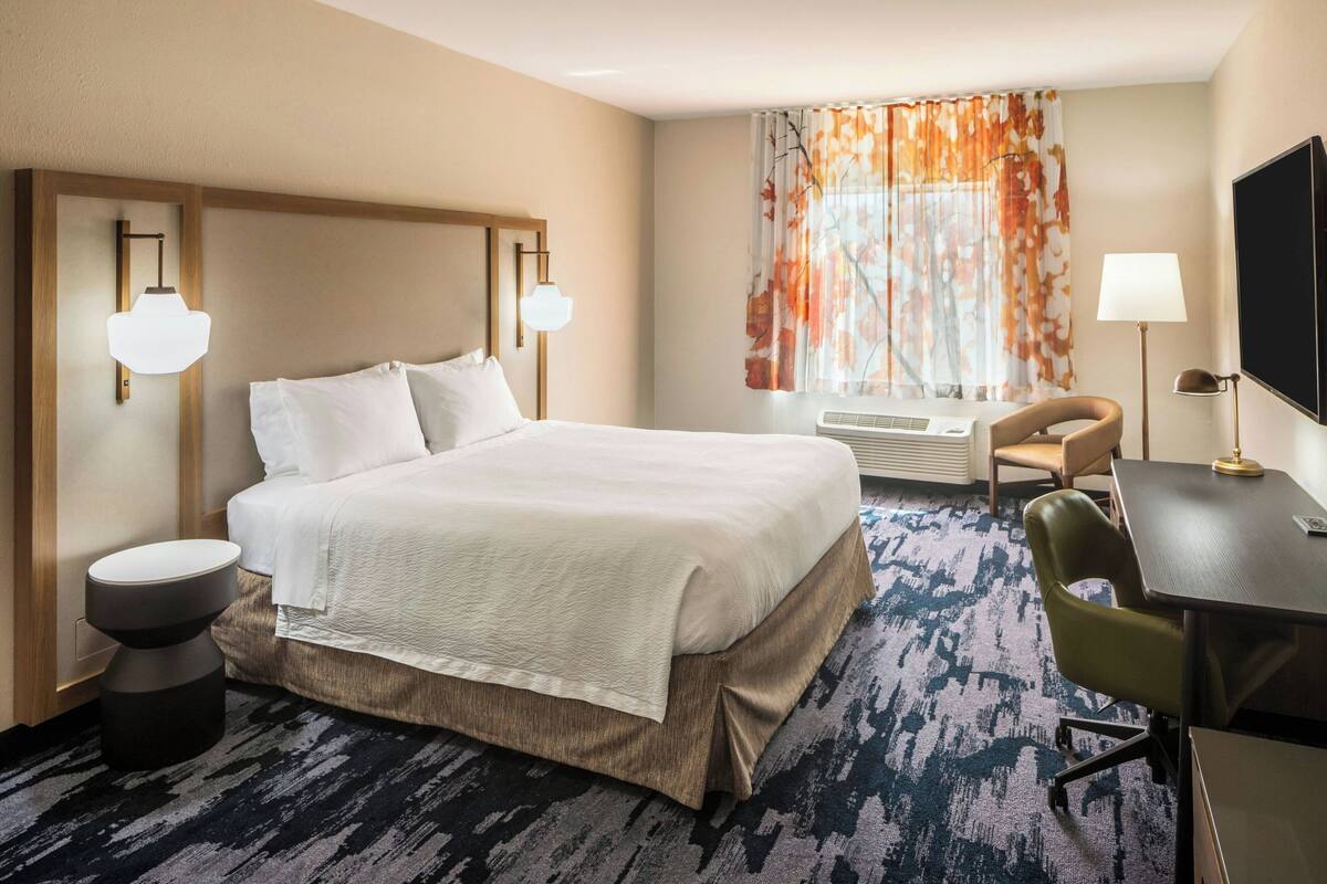 A hotel room with a large bed, a desk, a chair, a TV, and a window with curtains.