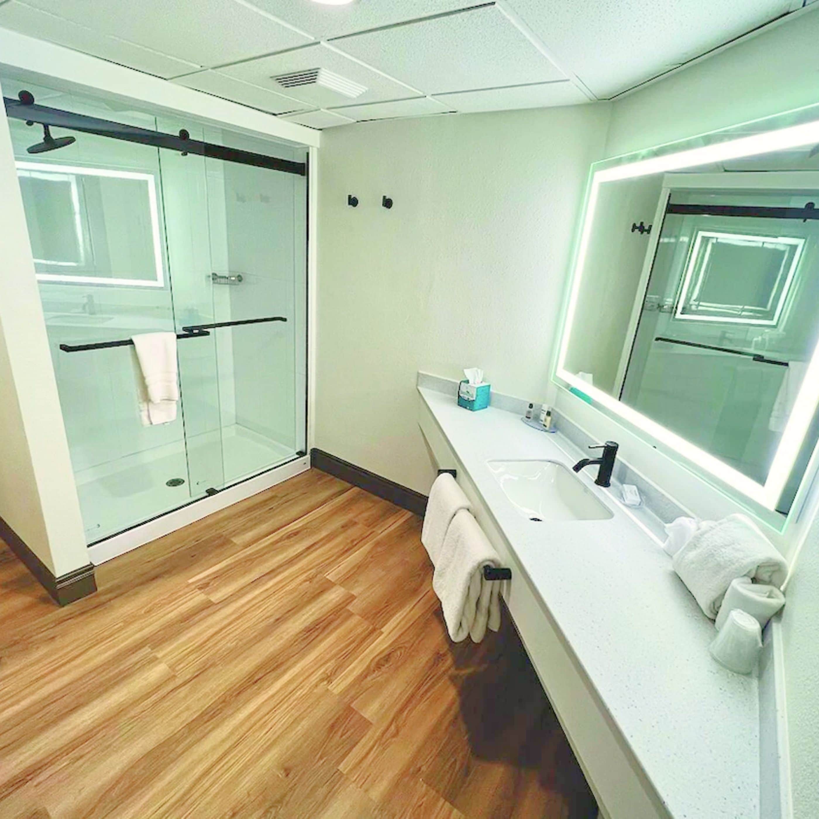 Un baño moderno con ducha de vidrio, un espejo grande y suelo de madera.