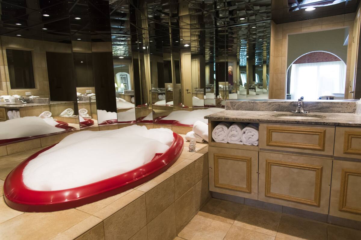 A modern bathroom with a large mirror, a red bathtub, and neatly folded towels.