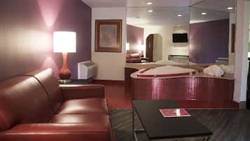 Ein Hotelzimmer mit einer Ledersofa, einem Tisch, einer roten Kachelbade-Wanne, einem Spiegel und einem Fernseher.