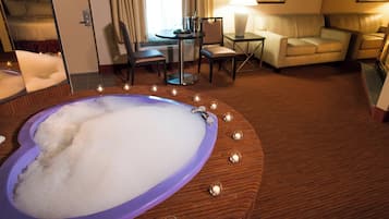 Een hotelkamer met een groot bad, een eethoek en een zithoek met een bank en lamp.
