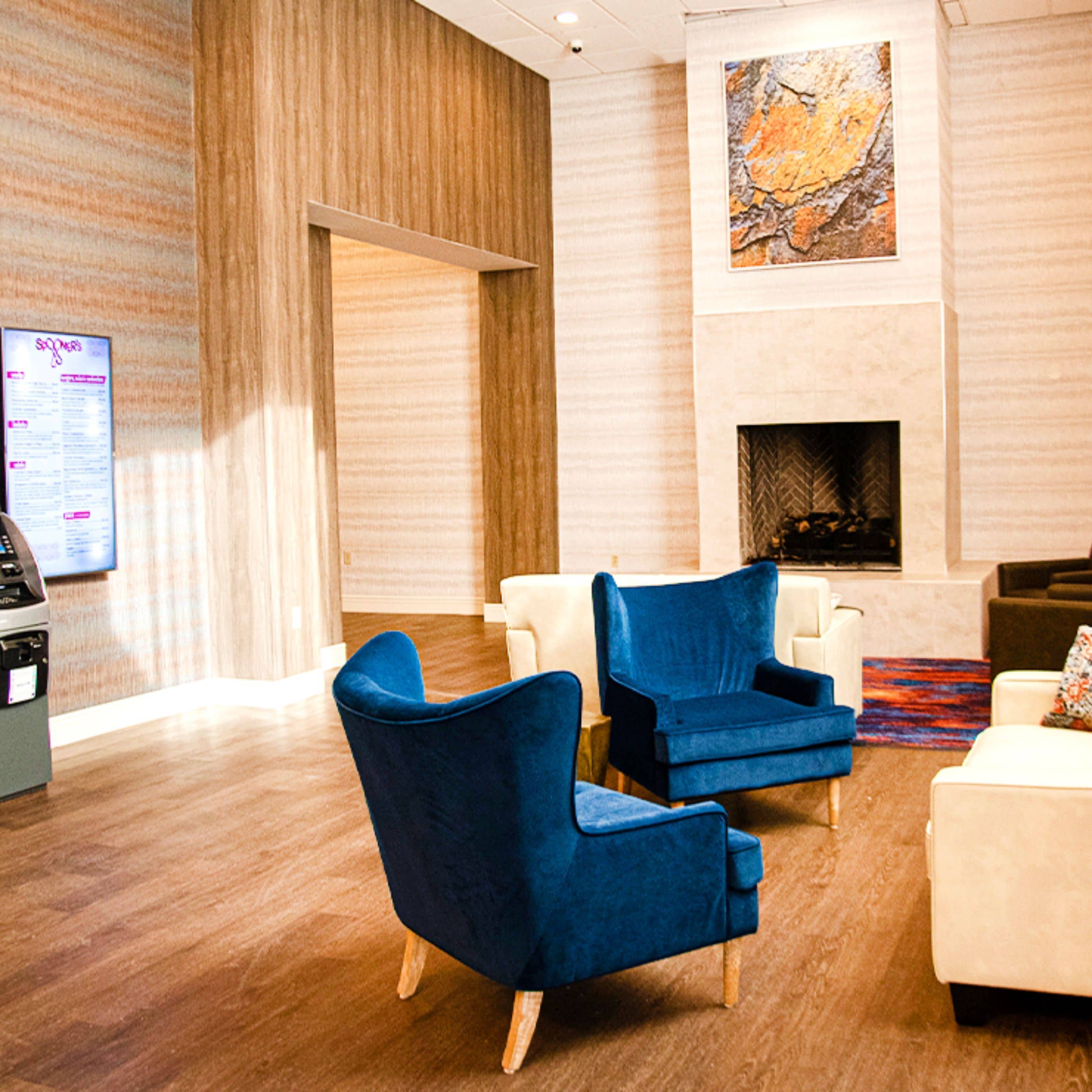 A modern lobby with a wooden floor, a fireplace, and seating areas with blue and white chairs.
