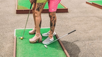 A couple playing mini-golf, with a heart-shaped sign in the background.