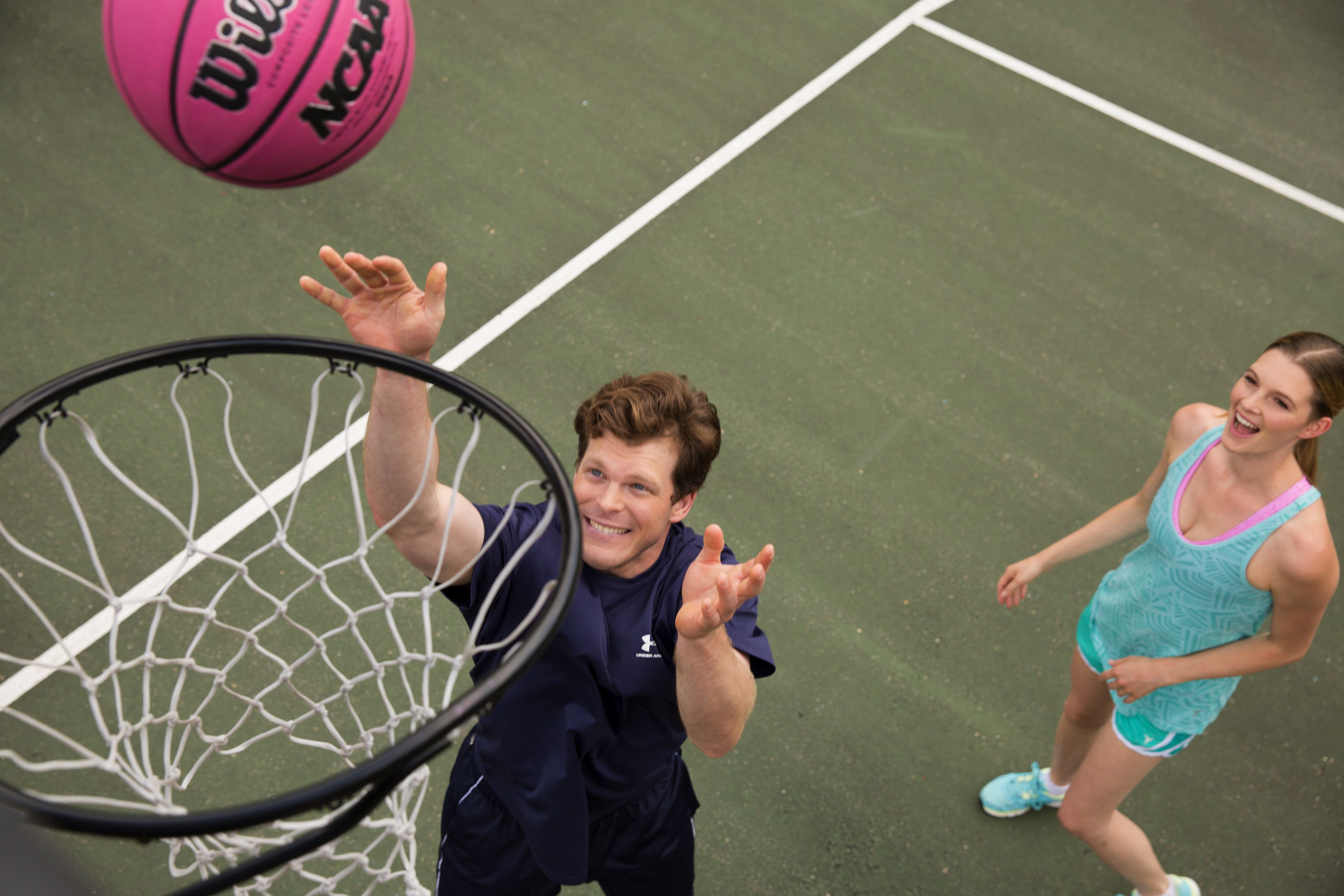 Un panier de basket avec un ballon rose, une personne portant un t-shirt bleu foncé et une autre personne portant un maillot de bain bleu clair.