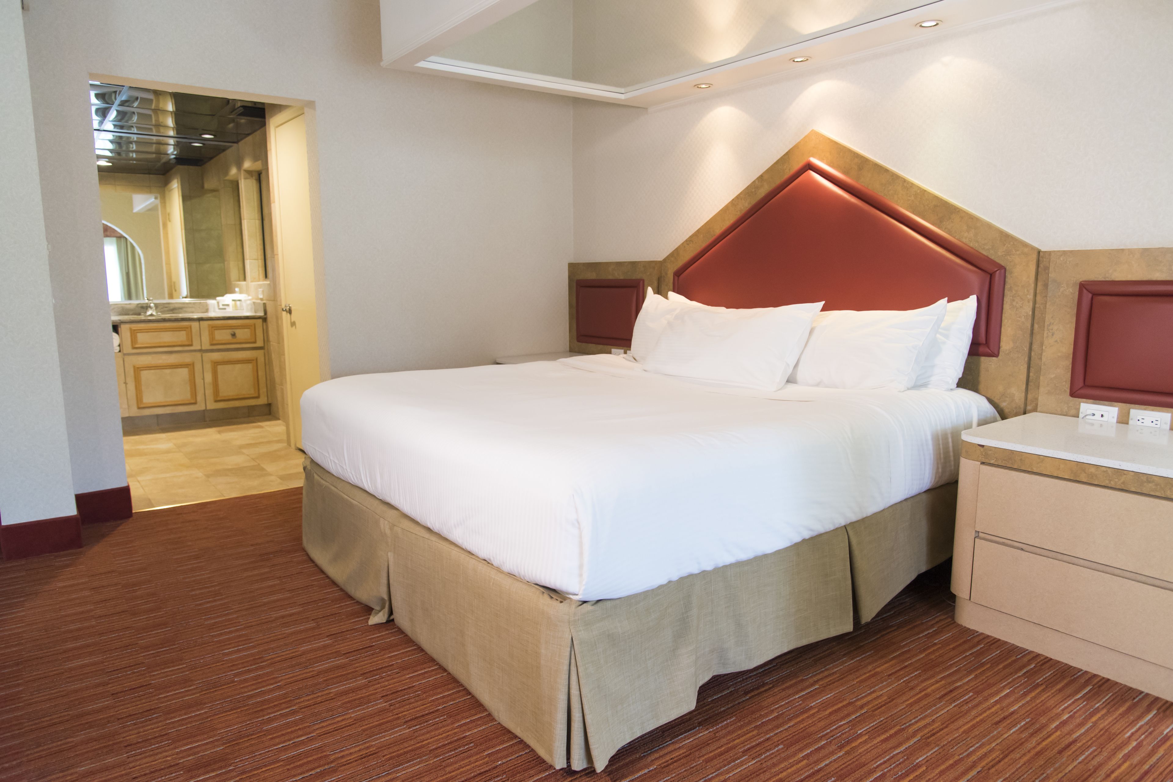 A hotel room with a large bed, a wooden floor, a kitchenette, and a bathroom visible through an open door.