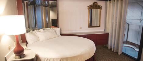 A hotel room with a large bed, a bedside lamp, a mirror, and a view of the outside.