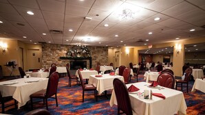 A banquet hall with multiple tables and chairs, a stone wall with a fireplace, and a carpeted floor.