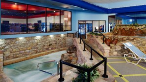 An indoor pool area with a stone wall, a hot tub, and a lounge chair. - Paradise Stream Resort (Cresco)