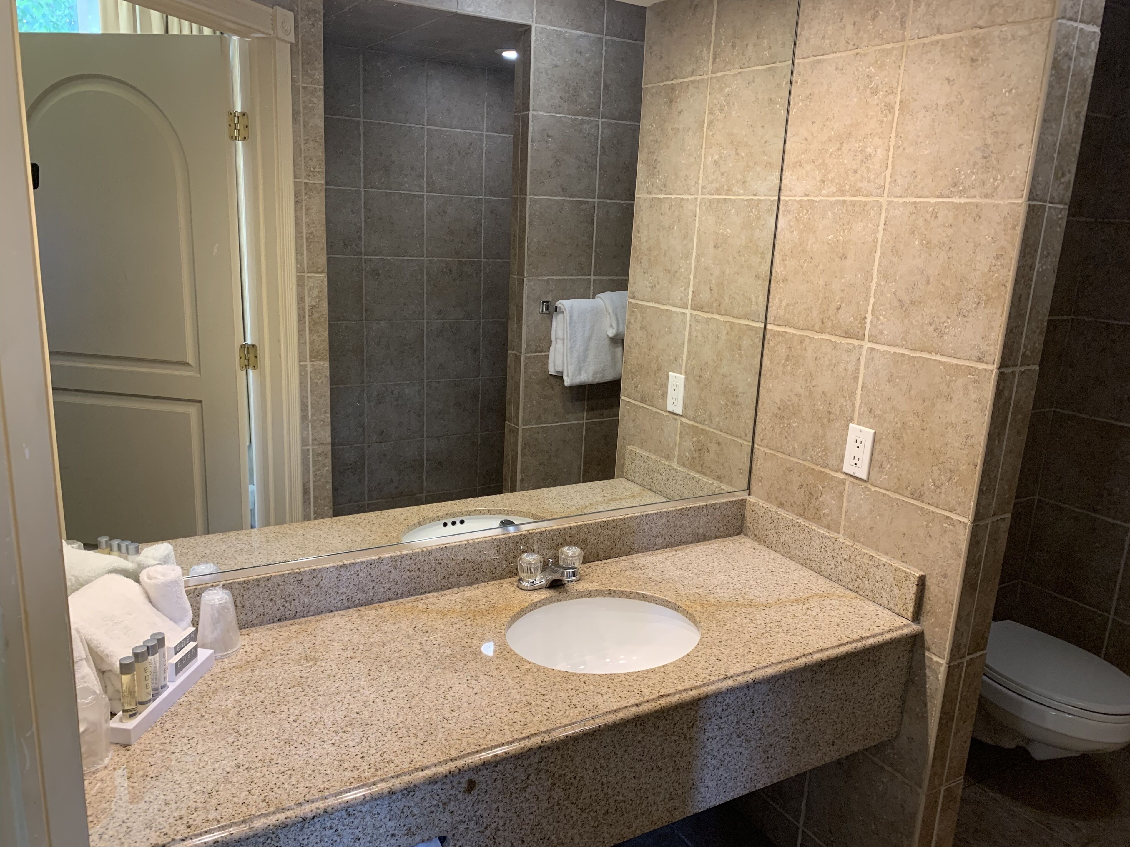 A bathroom with a granite countertop, a white sink, a mirror, and a toilet.