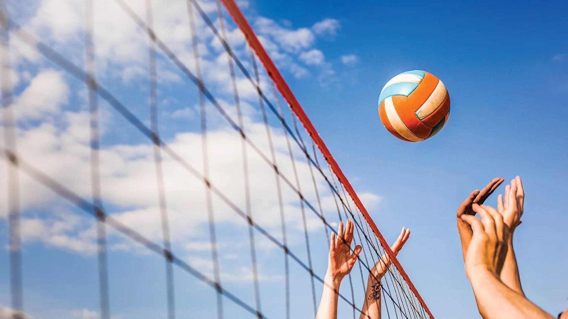 Partido de voleibol con jugadores intentando alcanzar la pelota bajo un cielo despejado.