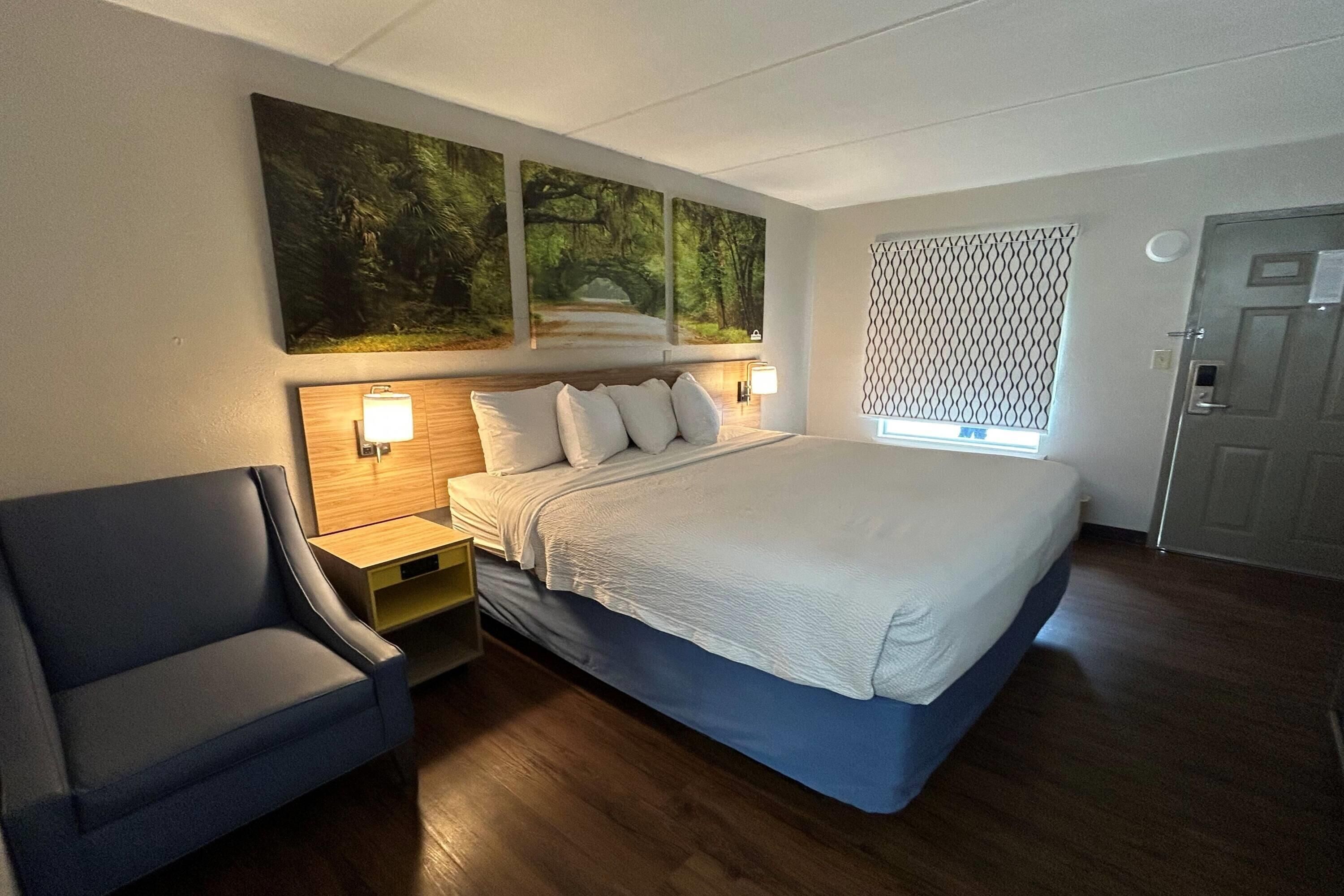 A bedroom with a bed, a chair, a nightstand, and wall-mounted artwork.