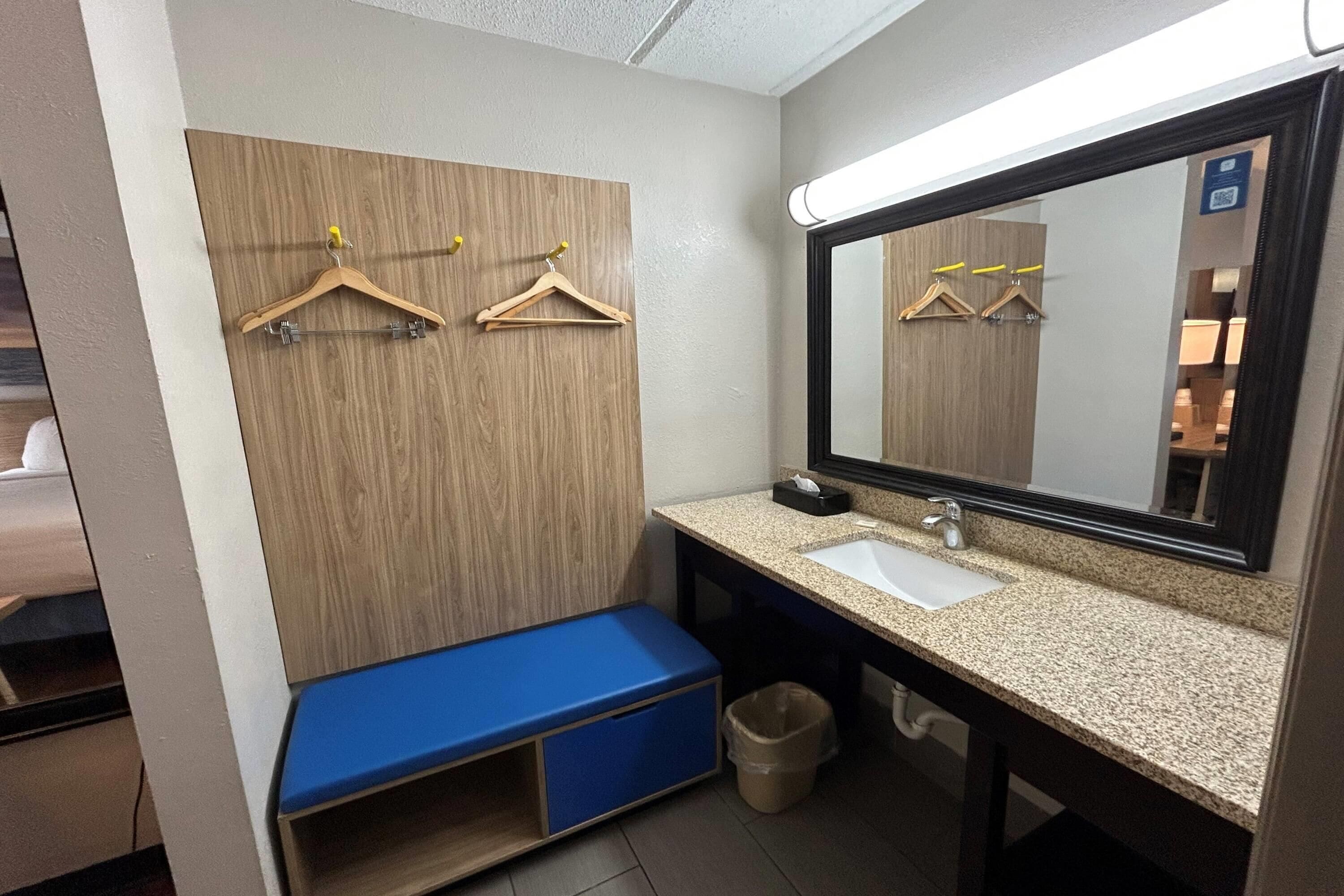 Un baño con pared de paneles de madera, un lavamanos, un espejo y un banco azul.