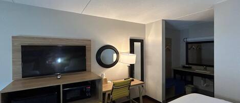 A hotel room with a bed, a desk with a chair, a television, a mirror, and a window.