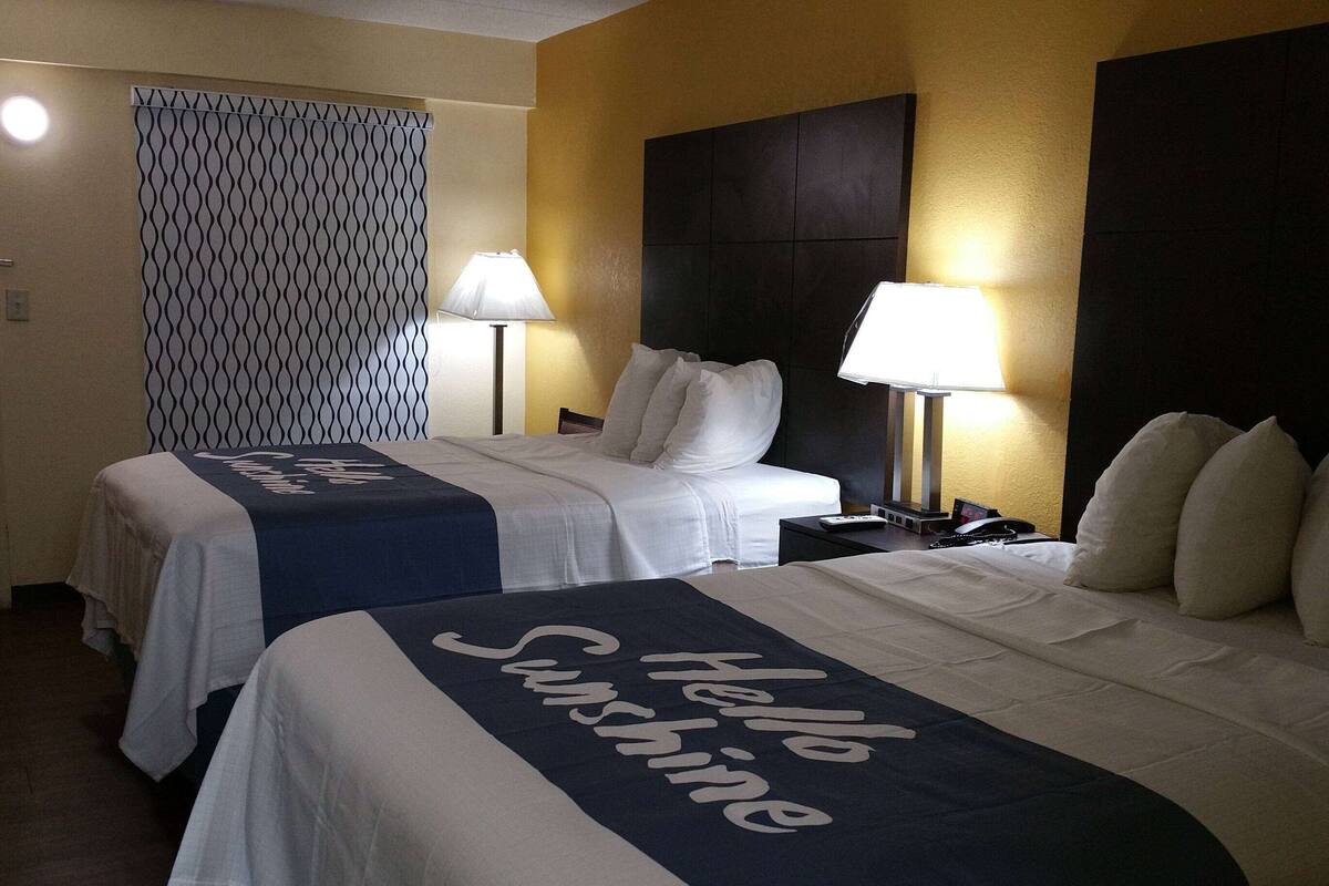 A hotel room with two beds, each with a headboard, a bedside table with a lamp, and a patterned curtain.