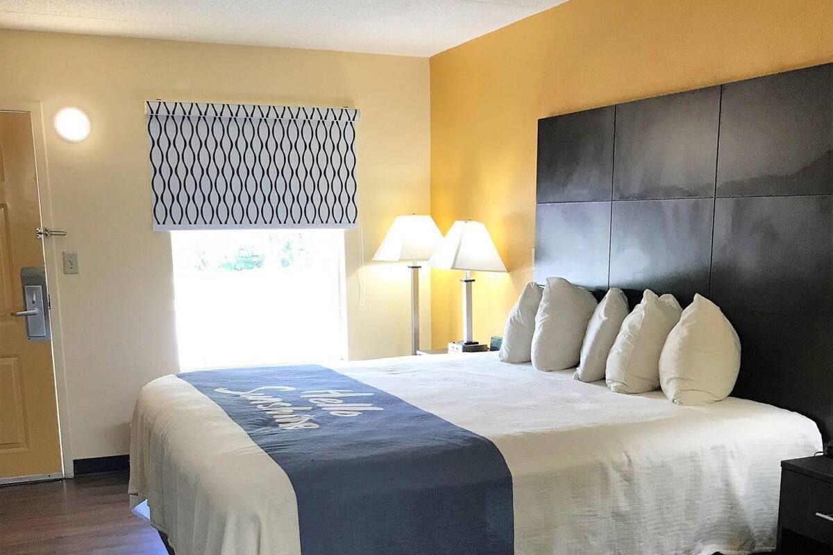 A hotel room with a bed, bedside lamps, a patterned window blind, and a door.