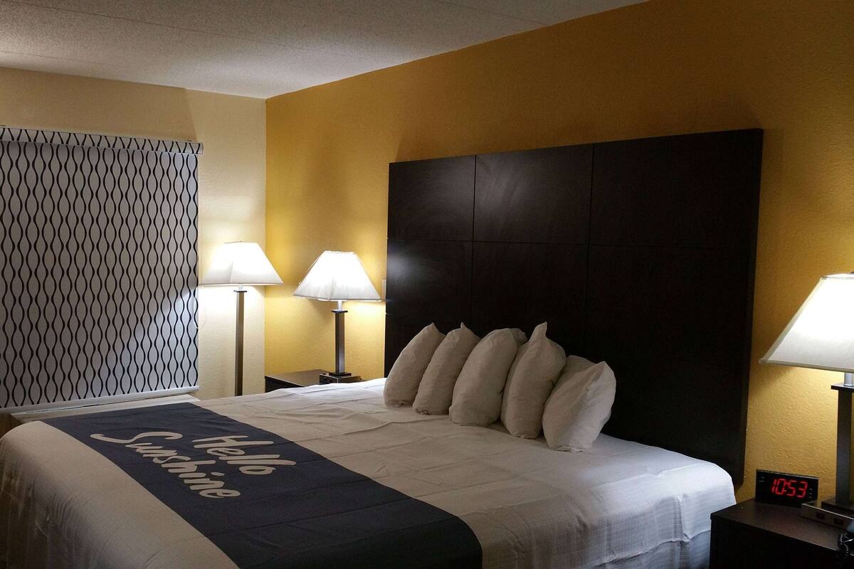 A hotel room with a bed, two bedside lamps, a digital clock, and a patterned wall.