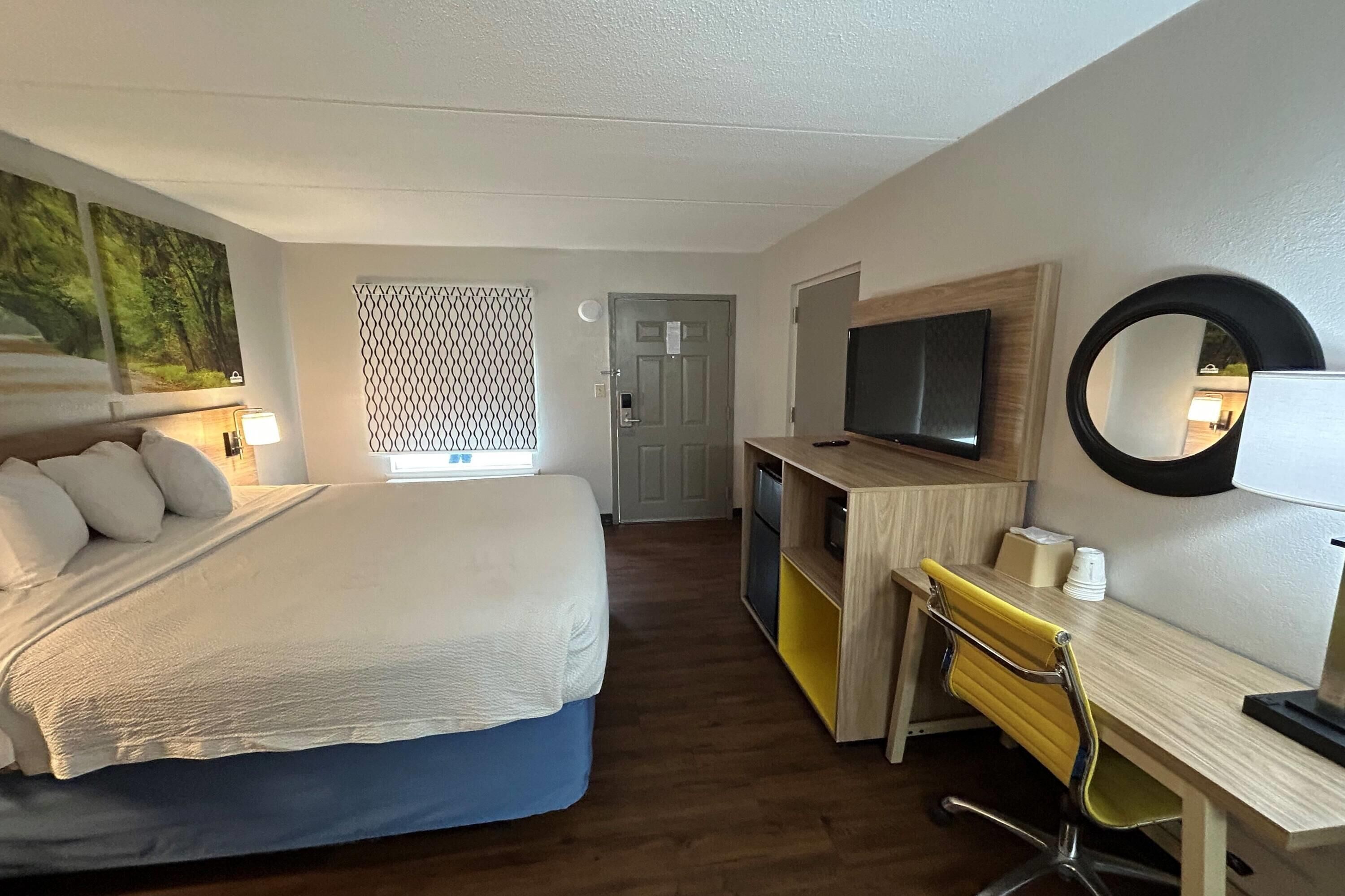 Una camera d'albergo con un letto, una scrivania, una sedia, una televisione e uno specchio.