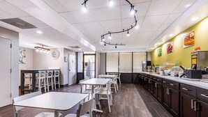 A modern restaurant interior with white tables and chairs, a long counter with a coffee machine, and a yellow accent wall. - Quality Inn Gordonsville (Gordonsville)
