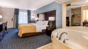A hotel room with a large bed, a separate bathroom with a bathtub, a desk with a chair, and a mirror. - Quality Inn Gordonsville (Gordonsville)