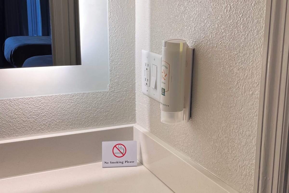 A bathroom with a white sink, a mirror, a "No Smoking" sign, and a wall-mounted electrical outlet.