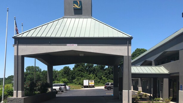 A covered parking area with a clear sky, a sign indicating a clearance of 13 feet, and a building with a distinctive logo on the roof. - Quality Inn Gordonsville (Gordonsville)