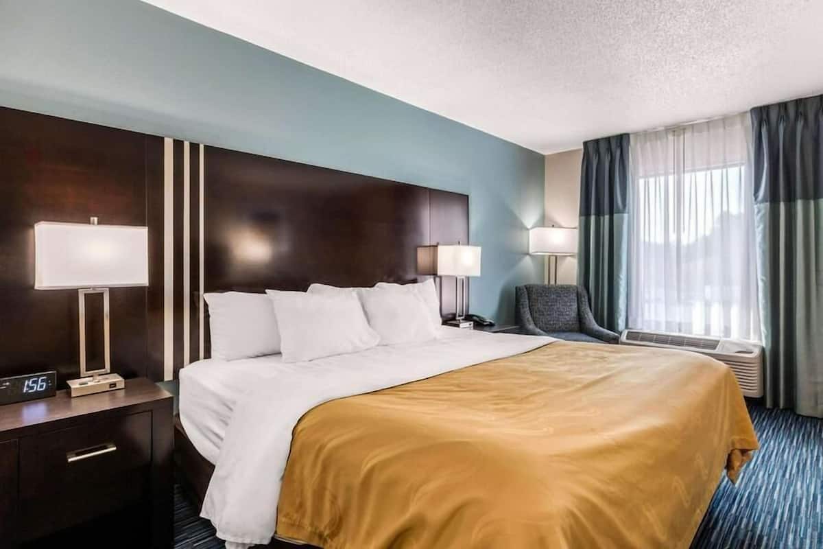 A hotel room with a large bed, two bedside tables with lamps, a chair, a desk, and a window with curtains.