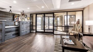 A reception area with a wooden reception desk, a seating area with a sofa and armchairs, and a large glass door leading to an outdoor space. - Quality Inn Gordonsville (Gordonsville)